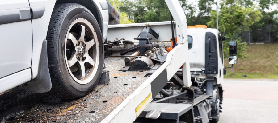 Cable attached to broken down car being pulled onto flatbed tow truck
